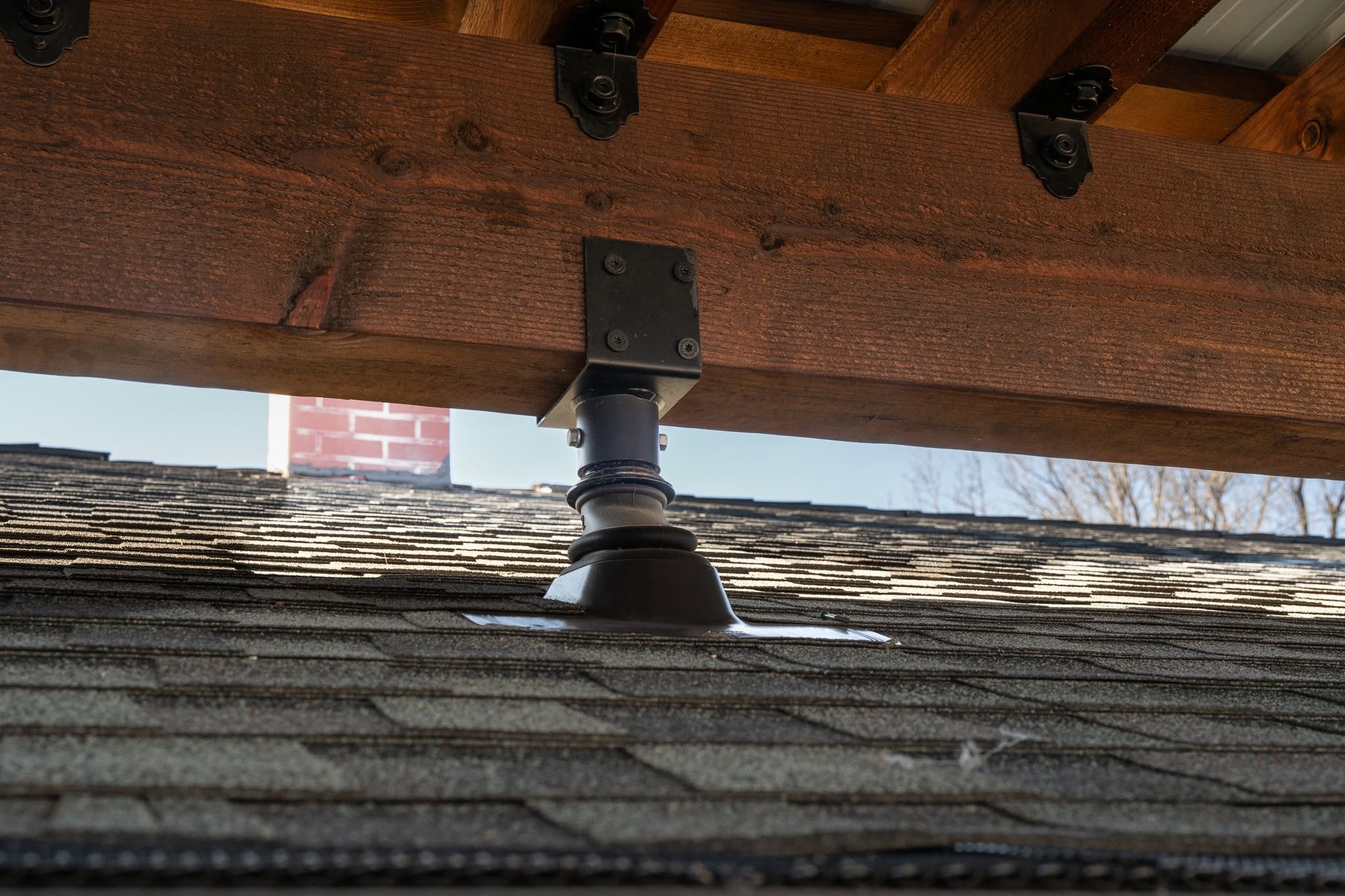 A wooden beam is supported by a metal bracket over a shingled roof.