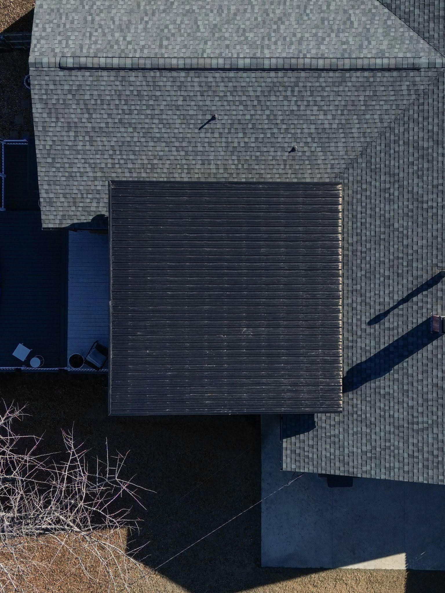 An aerial view shows a dark, flat-roofed addition attached to a grey, shingled house.